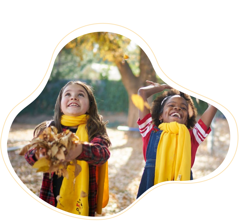 Two girls wearing yellow School Choice Week scarves throwing leaves into the air